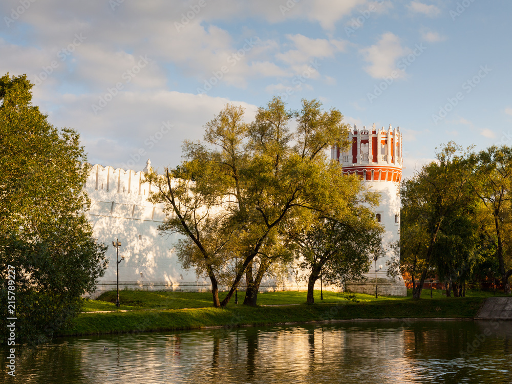 The walls and towers of the Novodevichy monastery in Moscow are reflected in the water in the summer evening before sunset