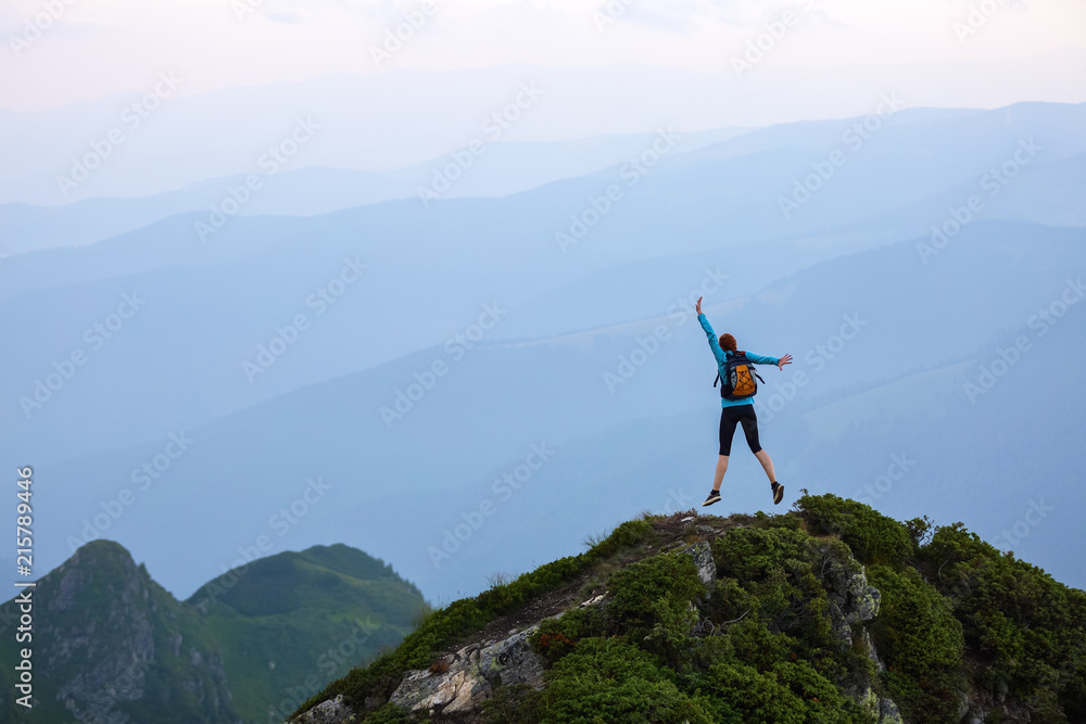 Funny frozen poses while jumping. The girl in tennis shoes. The lawn at the edge of the cliff with rocks. Vastness with mountains. Fantastic summer scenery.