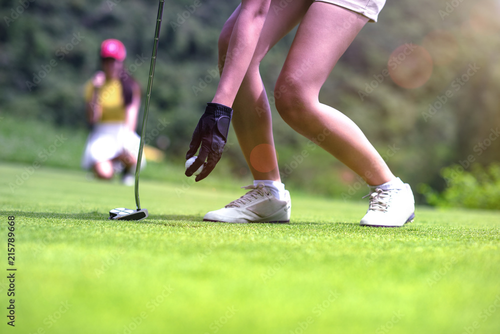 Obraz premium hand of young woman golf player holding a golf ball on the green, with golfmate or challenger competitor exciting or enforcement in background, exciting or enforcement between players
