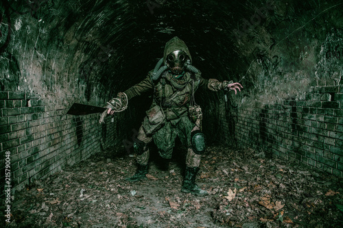 Post apocalyptic mutant creature or survivor in tatters and gas mask jumps out of darkness and attacking with handmade machete in abandoned tunnel  frightening dungeon or city old sewage collector