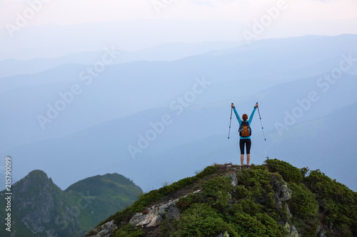 The tourist girl with the tracking sticks and the back sack at the edge of the cliff. The landscape with the high mountains. Endless vastness on the horizon. Warm sunny summer day.