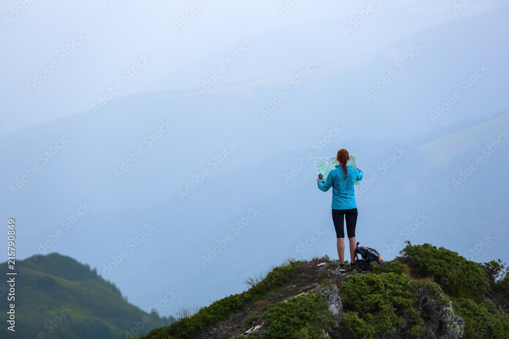 On the peak of the mountain the touris girl with the map and compass is searching for the way to dream. The horizon in the fog. Summer scenery. Extreme sport.