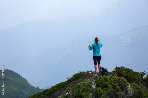 On the peak of the mountain the touris girl with the map and compass is searching for the way to dream. The horizon in the fog. Summer scenery. Extreme sport.
