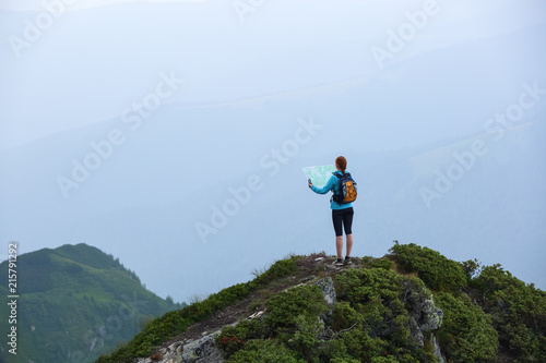 On the peak of the mountain the touris girl with the map and compass is searching for the way to dream. The horizon in the fog. Summer scenery. Extreme sport. © Vitalii_Mamchuk