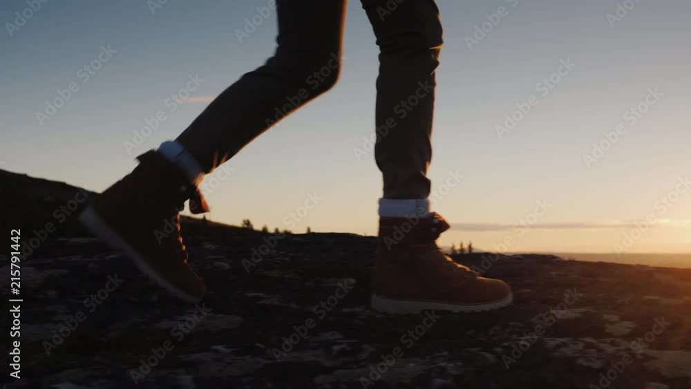 Legs in trekking boots go along the mountain ridge against the backdrop of the rising sun. Travel and adventure concept