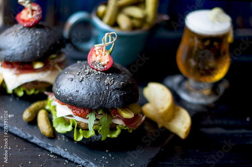 Black hamburger with beef, salad and French fries. Fresh beer in a glass. Trends of street food. A calorie dinner. Copy space.