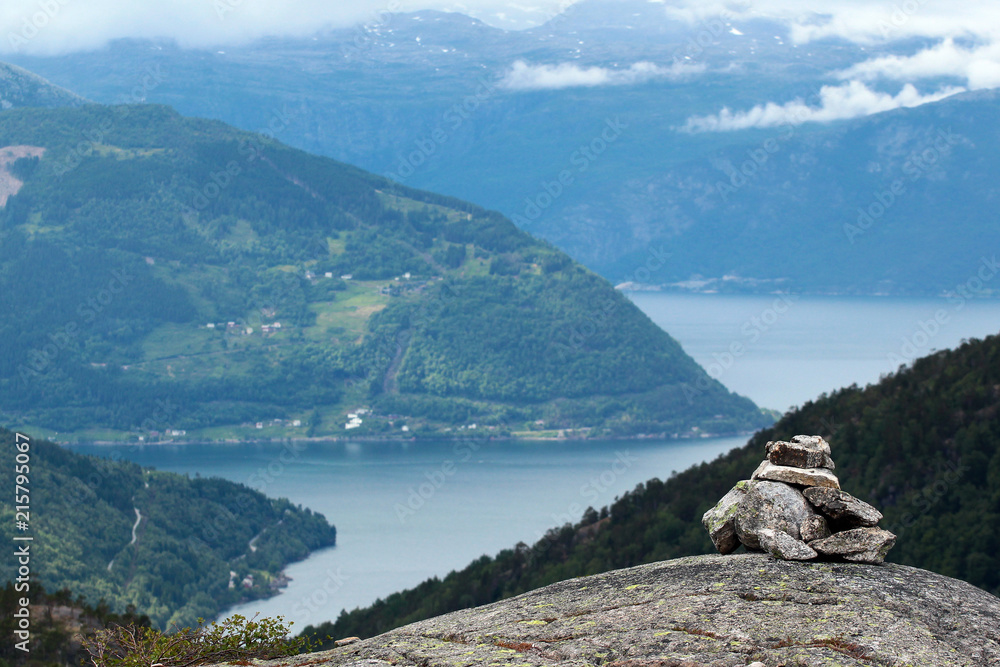 Stone cairn in Husedalen valley with cascade of four waterfalls, Kinsarvik, Norway