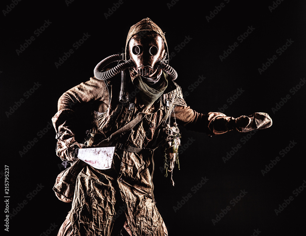 Low key portrait of post apocalyptic creature, living in catacombs mutant,  survived in nuclear disaster human in ragged cloth and gas mask, armed with  handmade cold weapon isolated on black background Stock