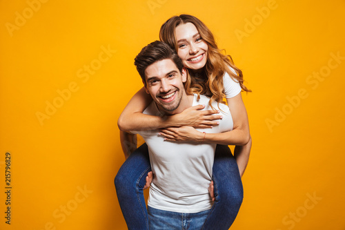 Image of lovely couple having fun while man piggybacking his girlfriend, isolated over yellow background photo