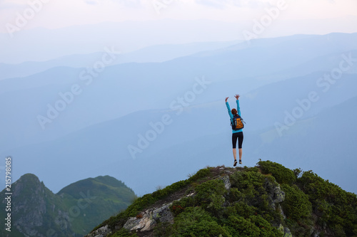 Funny frozen poses while jumping. The girl in tennis shoes. The lawn at the edge of the cliff with rocks. Vastness with mountains. Fantastic summer scenery.