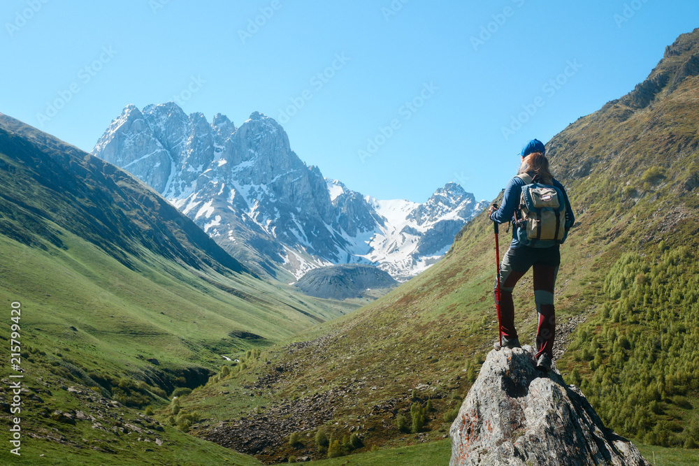 Woman with Backpack and trekking sticks look view of the mountain range