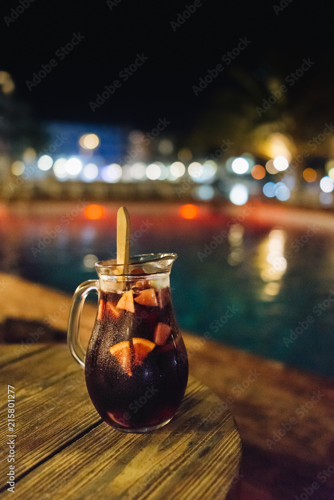 Sangria carafe on the wooden table at night by the pool