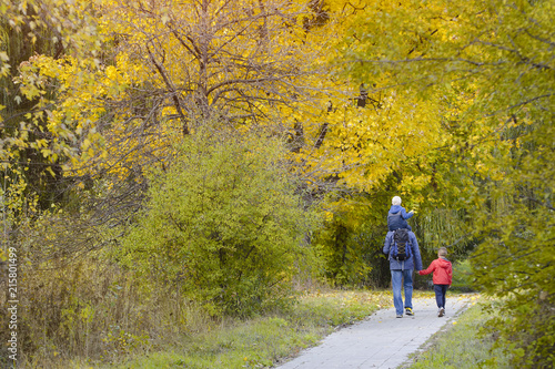 Father and two sons walk through the autumn park. Back view