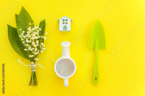 Flat Lay gardening tools, watering can, shovel, rake, flowers and toy house on yellow colourful trendy background. Spring or summer in garden, eco, nature, farm, horticulture hobby concept photo