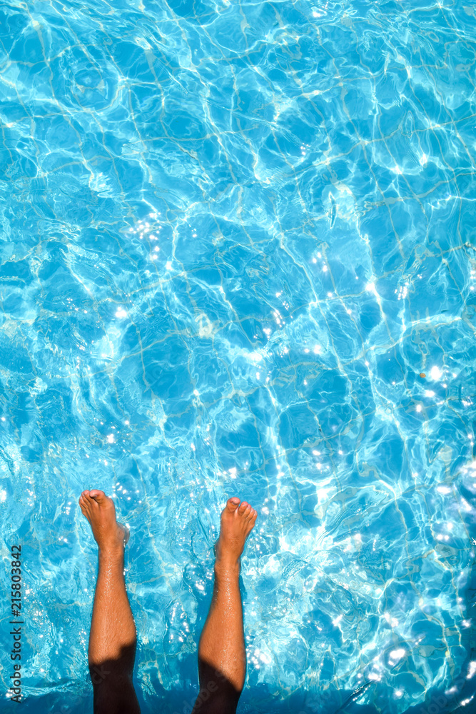 man's feet against blue water of the pool, feet in the pool
