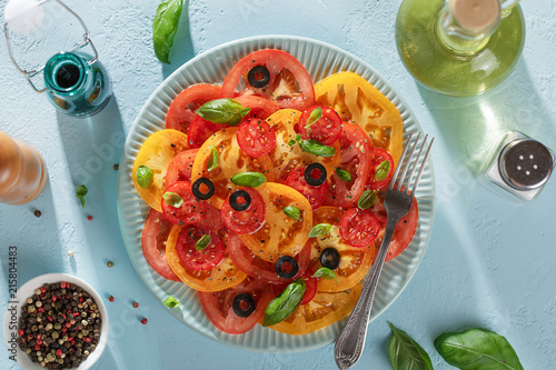 Homemade tomato carpaccio on blue plate with fork, balsamic sauce, oil and spices on blue table.