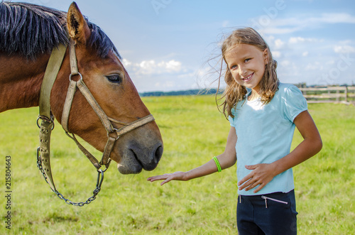 girl in blue t-shirt feeding horse with palm cookie in summer