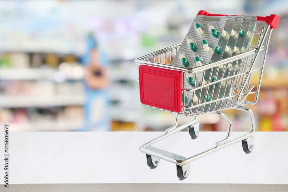 medicine pills capsule in shopping cart on pharmacy store counter with blur drugstore shelves defocused background medicine pills capsule in shopping cart on pharmacy store counter with blur drugstore shelves defocused background