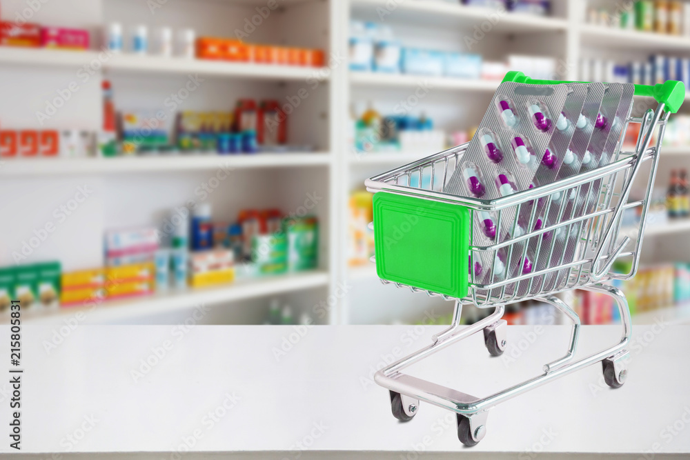 medicine pills capsule in shopping cart on pharmacy store counter with blur drugstore shelves defocused background