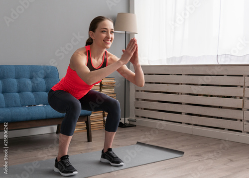 Happy fitness woman doing squat exercise at home photo