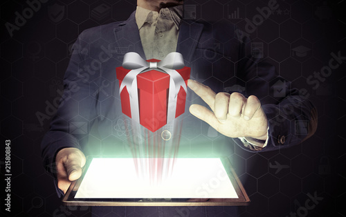 A man is holding a tablet pc. She clicks on the gift. Concept of gift giving, choice of gifts.