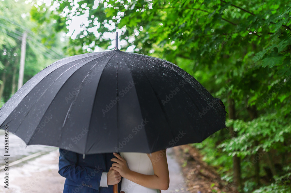Loving couple take shelter together beneath an umbrella in the rain.