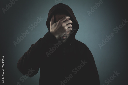 Desperate hooded man covering his face on dark room.
