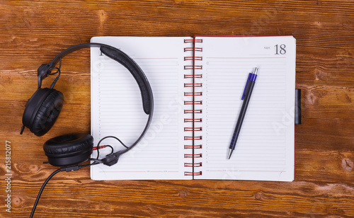 Blank notepad with a pen and headphones on vintage wooden table background. Notepad, pencil and headphones. Top view.