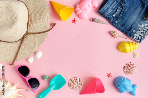Baby Girl's accessories for the beach. Straw hat, sunglasses, sand molds, shorts, swimsuit, cockleshells on a pink background. View from above.