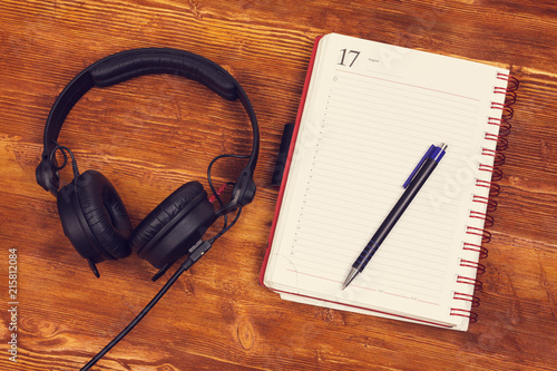 Blank notepad with a pen and headphones on wooden table background. Notepad, pencil and headphones. Top view. insta look