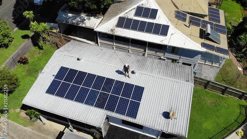 Aerial shot of solar panel technician with drill installing solar panels on roof on a sunny day