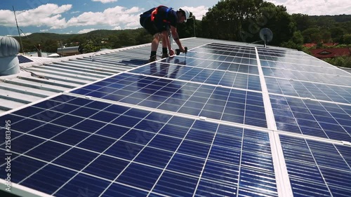 Solar panel technician with drill installing solar panels on roof on a sunny day