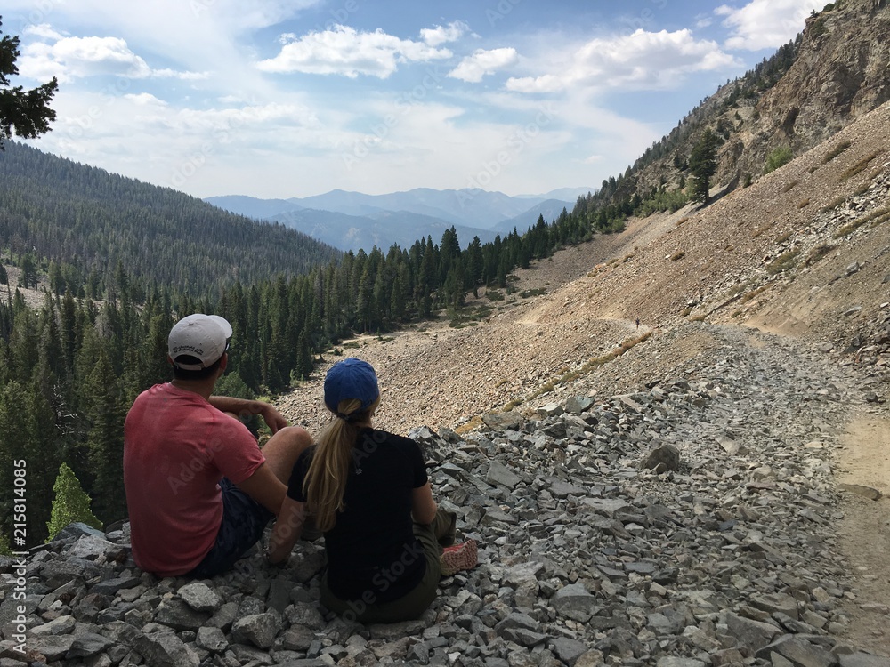 A couple sits on a mountain looking at trees and rocks 