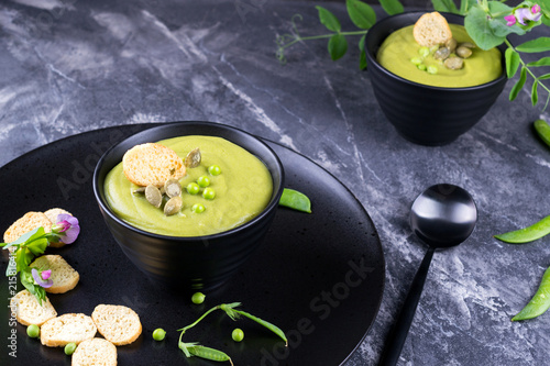 Light summer delicious green peas cream soup served with pumpkin seeds, croutons on dark background.