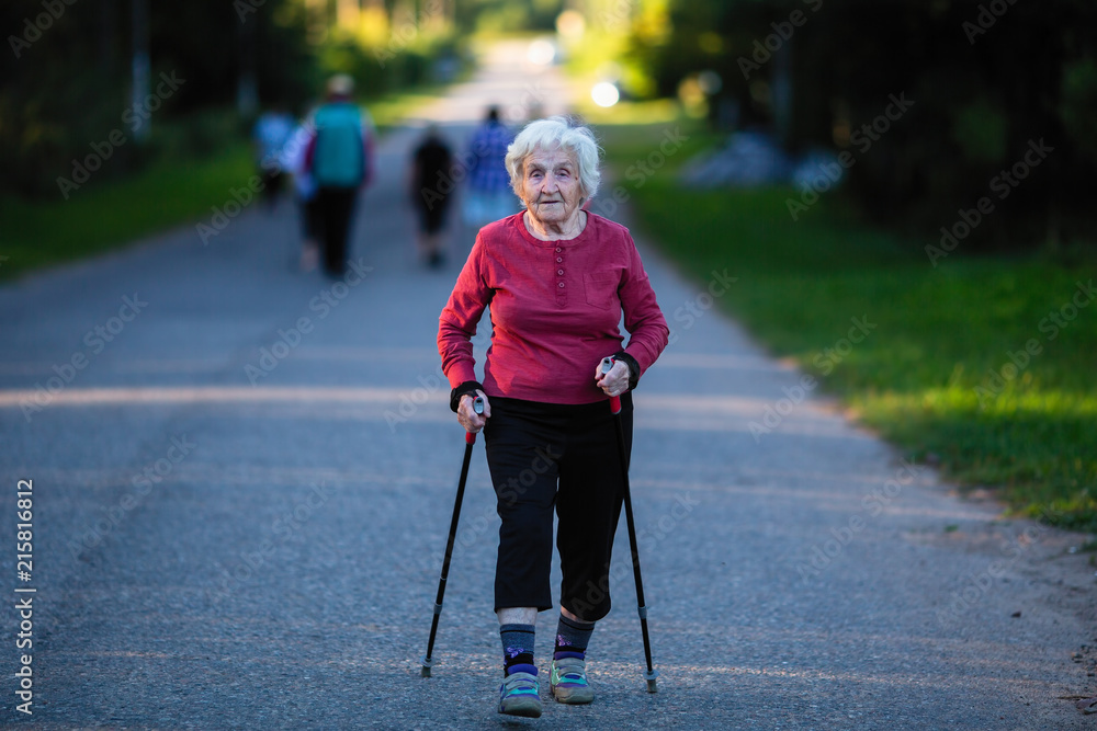 Nordic walking. An elderly woman with ski poles is on the road.