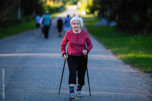 Obraz na płótnie Nordic walking. An elderly woman with ski poles is on the road. w salonie