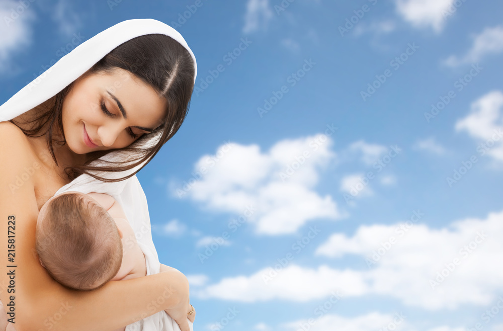 family, breastfeeding and motherhood concept - happy young mother with little baby sucking breast over sky background family, breastfeeding and motherhood concept - happy young mother with little baby sucking breast over sky background