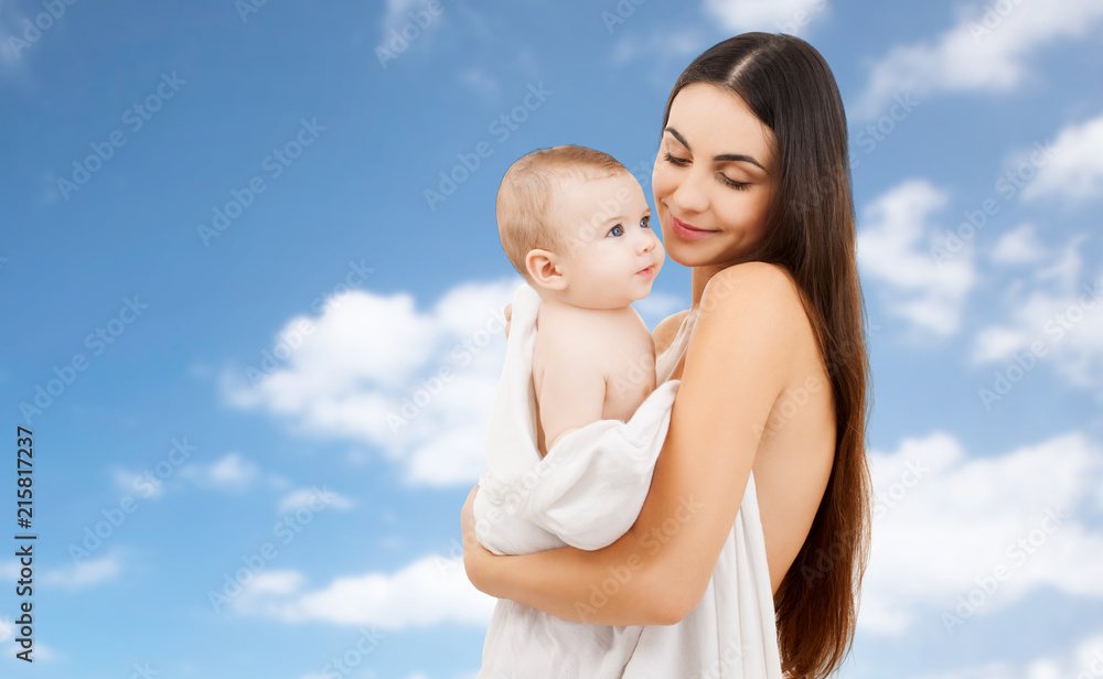 family and motherhood concept - happy smiling young mother with little baby wrapped into bath towel over sky background family and motherhood concept - happy smiling young mother with little baby wrapped into bath towel over sky background