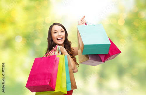people and sale concept - young smiling woman with shopping bags over green background and lights