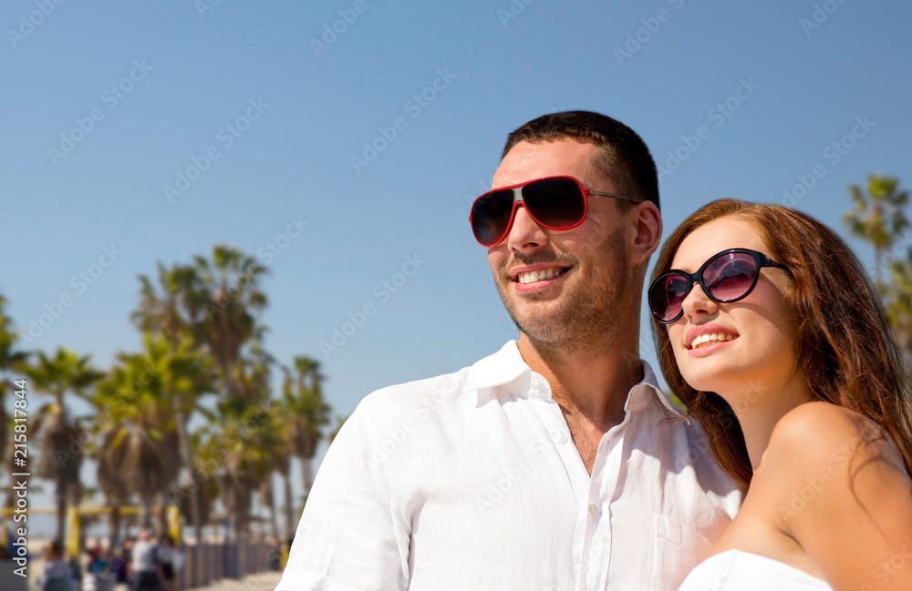 travel, tourism and summer concept - happy smiling couple in sunglasses over venice beach background in california