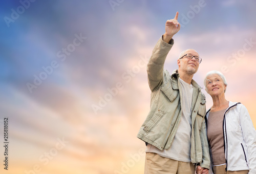 old age, tourism, travel and people concept - happy senior couple holding hands over evening sky background