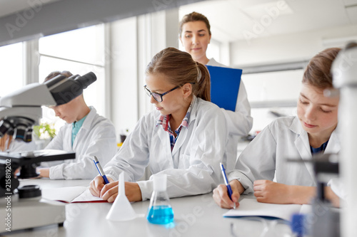 education  science and children concept - teacher and students studying chemistry at school laboratory and writing to workbooks