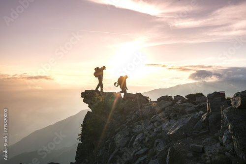 Two Backpackers hiking on a mountain close to a cliff, with camping equitment and a beautiful view on the sunrise (exploring and travel adventure)