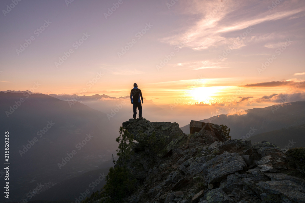 Young man standing on the Top of the mountain and enjoying total freedom during sunset in South Tyrol
