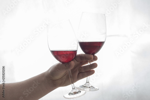 hand holding two wineglasses with red wine