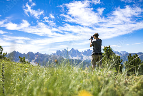 A youg guy taking picture of the Geisler mountains on the plose (Italian Dolomites)