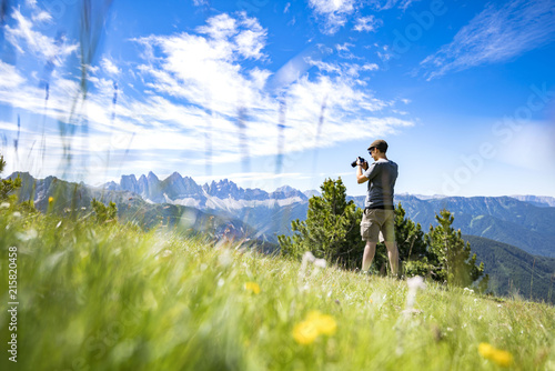 A youg guy taking picture of the Geisler mountains on the plose (Italian Dolomites)