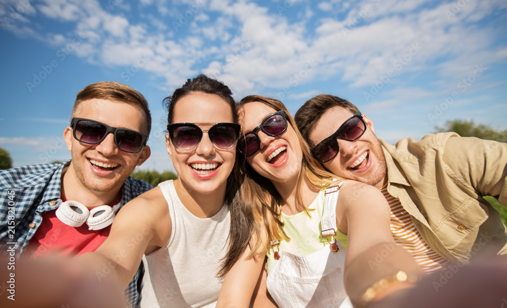 leisure, people and friendship concept - happy teenage friends taking selfie outdoors in summer
