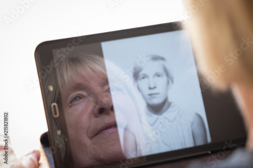 Senior caucasian woman looking at old photos of herself as a young woman on a tablet computer themes of contrasts the ageing process nostalgia and childhood