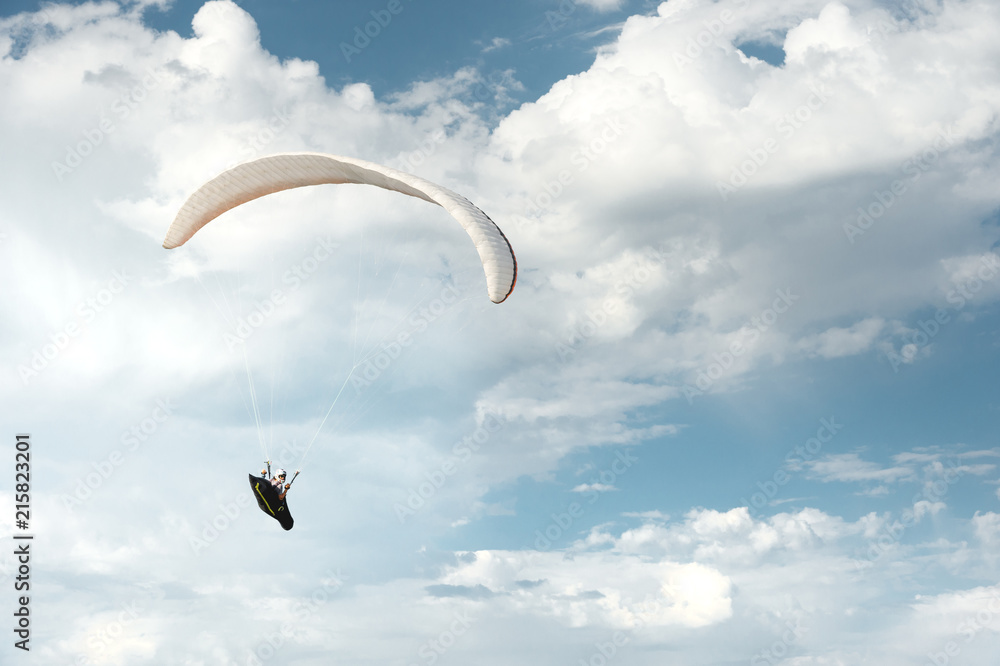 Professional paraglider flies on a white paraglider against the blue sky and white clouds. Paragliding sport Professional paraglider flies on a white paraglider against the blue sky and white clouds. Paragliding sport
